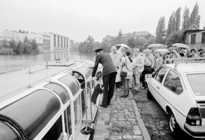 Menschen steigen bei Regen an einem Anleger in ein Boot, Schwarzweißfoto