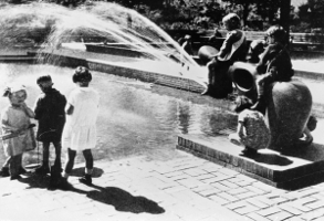 Kinder spielen an einem Brunnen mit Figuren, Wasserstrahlen spritzen