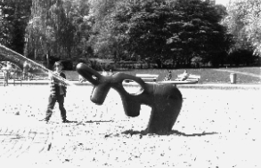 Kind spielt mit Wasserspritzfigur auf einem Spielplatz, Schwarzweißaufnahme