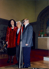 Drei Personen stehen nebeneinander auf Bühne in einer Kirche, Mikrofon vorn