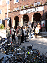 Menschen stehen in Reihe vor dem Kino ‚Magazin‘, Fahrräder im Vordergrund