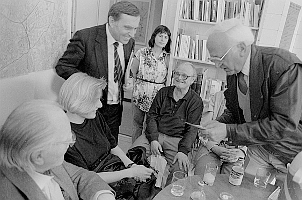 Gruppe im Gespräch an einem Tisch, Bücherregal im Hintergrund, Schwarzweißfoto
