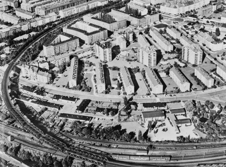Schwarzweißes Luftbild einer Nachkriegssiedlung mit Neubauten und Bahngleisen.