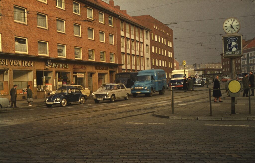 Straßenszene mit alten Autos, Geschäften und Uhr, mit Straßenbahnhaltestelle